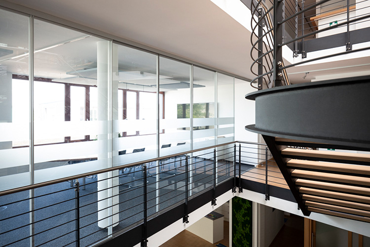 Treppenhaus und großer Besprechungsraum mit ovalem Tisch getrennt durch eine Glastrennwand mit Schiebetüren aus klarem Glas