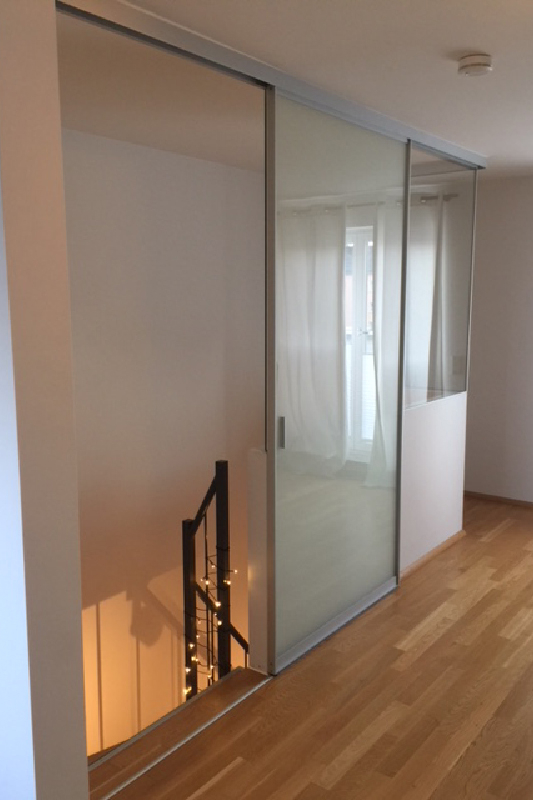 Wohnraum mit Treppenaufgang unterteilt durch Raumteiler Schiebetür aus mattem Glas